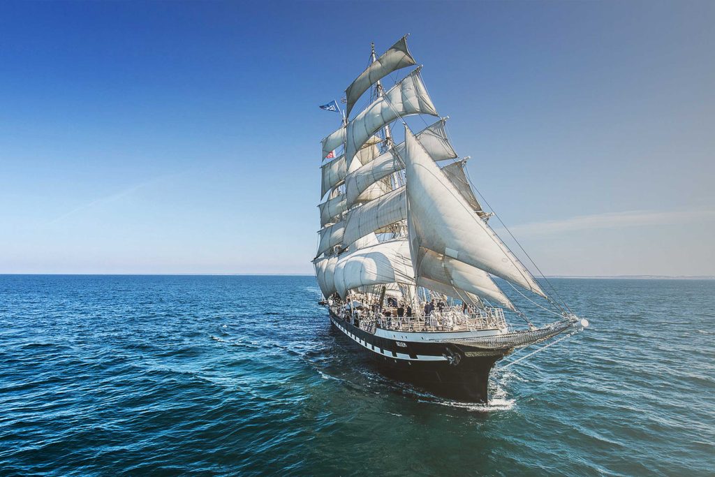 Le Belem de face qui fend une mer calme, voiles toutes déployées. La photo est prise depuis la mer.