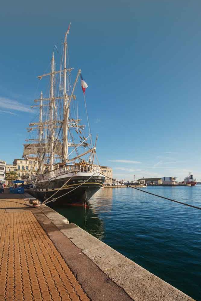 Le Belem à quai sur le port de Sète, par beau temps. Photo prise depuis le quai montrant majoritairement la proue du bateau.