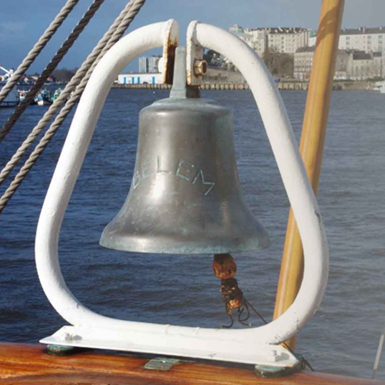 La cloche en fer du belem, sur une barrière du pont. Elle est entourée d'un sceau blanc. Chantenay est visible en fond.