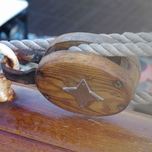 Gros plan sur une poulie de cordage en bois du Belem, fixée sur une barrière du bateau. Une étoile métallique à quatre branches est visible sur la poulie.